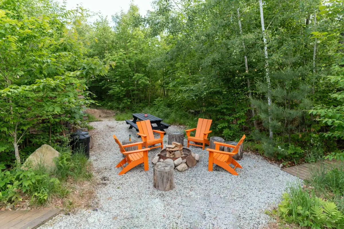 Fire pit seating area in woodland with adirondack chairs on gravel